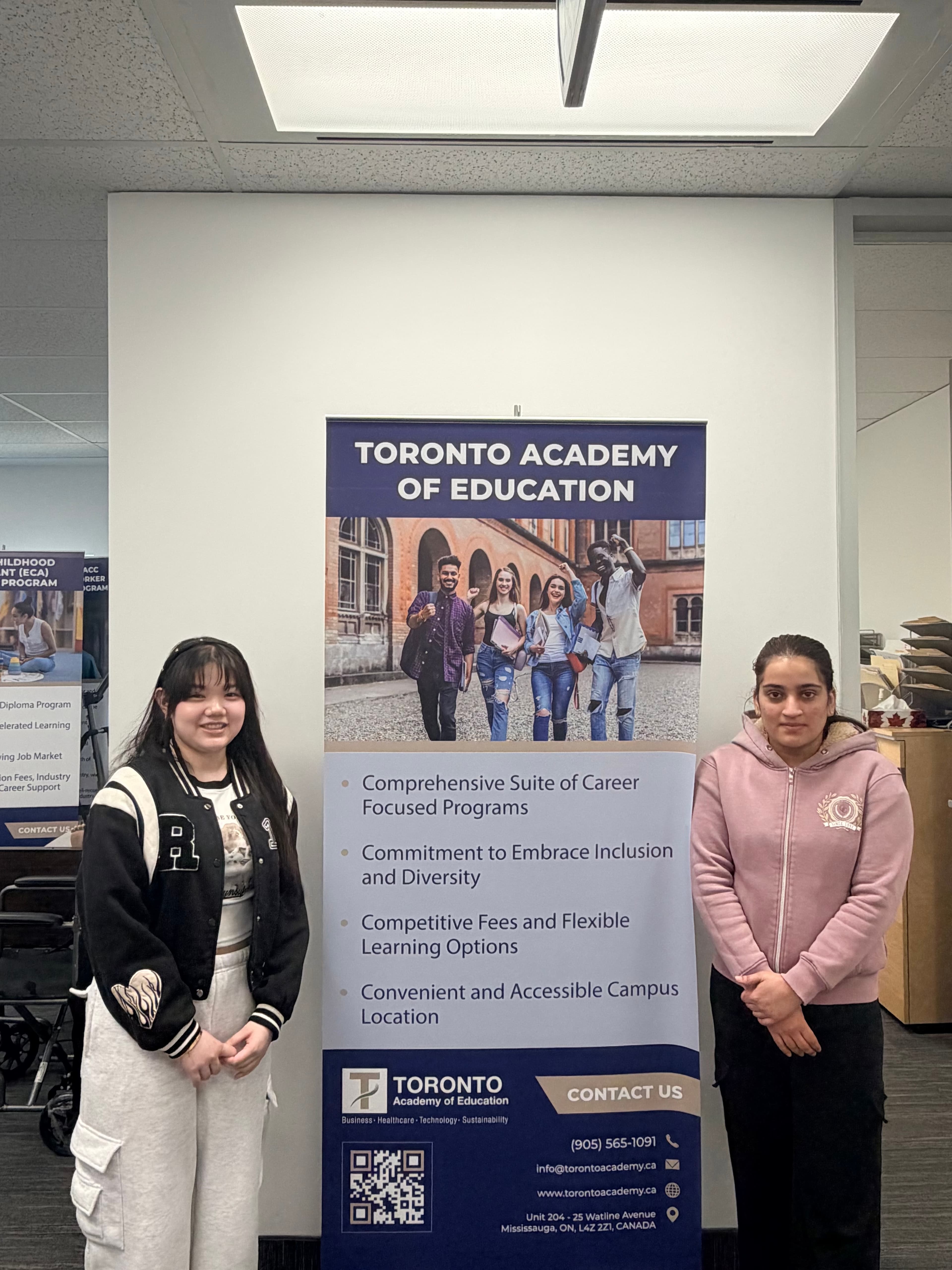 Two students standing beside a Toronto Academy of Education banner