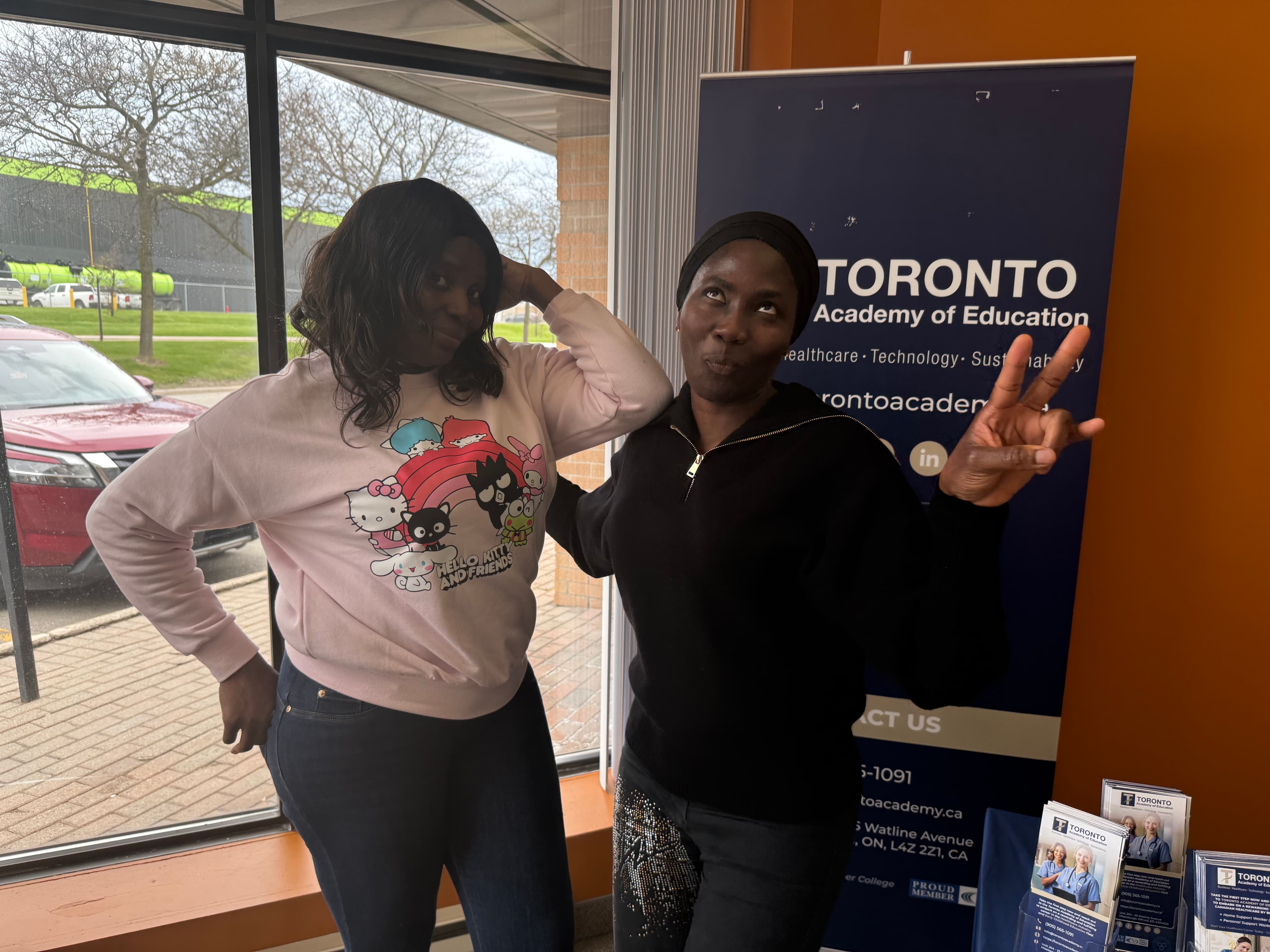 Two students posing in front of a Toronto Academy of Education banner